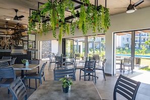 Un espace de restauration intérieur moderne, doté de tables et de chaises, de plantes suspendues et de grandes fenêtres.