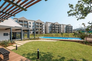 Un immeuble d’appartements moderne doté d’une piscine, d’un espace extérieur couvert avec des sièges et d’une pelouse bien entretenue.