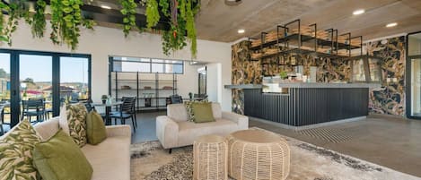 A modern interior with a sofa, wicker ottoman, ceiling fan, and indoor plants.
