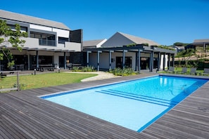 Un espace piscine moderne avec une terrasse en bois, une piscine à l’eau cristalline et un coin salon abrité.