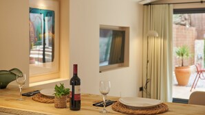 A dining table with a wine bottle, glasses, and plates, set against a wall with framed artwork and a view of the outdoors. - Studio Suite with private patio in Aiguablava-Begur (CT)