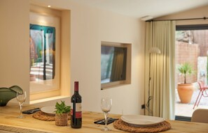 A dining table with a wine bottle, glasses, and plates, set against a wall with framed artwork and a view of the outdoors. - Studio Suite with private patio in Aiguablava-Begur (CT)