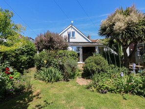 A house with a covered porch, surrounded by a garden with various plants and flowers.