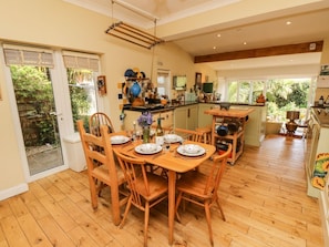A spacious kitchen with wooden flooring, a dining area with a table set for four, and a view of the garden through the sliding doors.