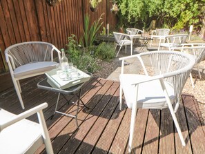 An outdoor patio with white wicker chairs and a table, surrounded by a wooden deck and greenery. - Querc, Stoney Middleton (Hope Valley)