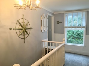 Un escalier avec une rampe blanche, une décoration murale en forme de boussole et une fenêtre avec des stores.