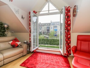 Uma sala de estar com um sofá vermelho, um sofá bege, um tapete vermelho e uma porta de vidro que dá para uma varanda.