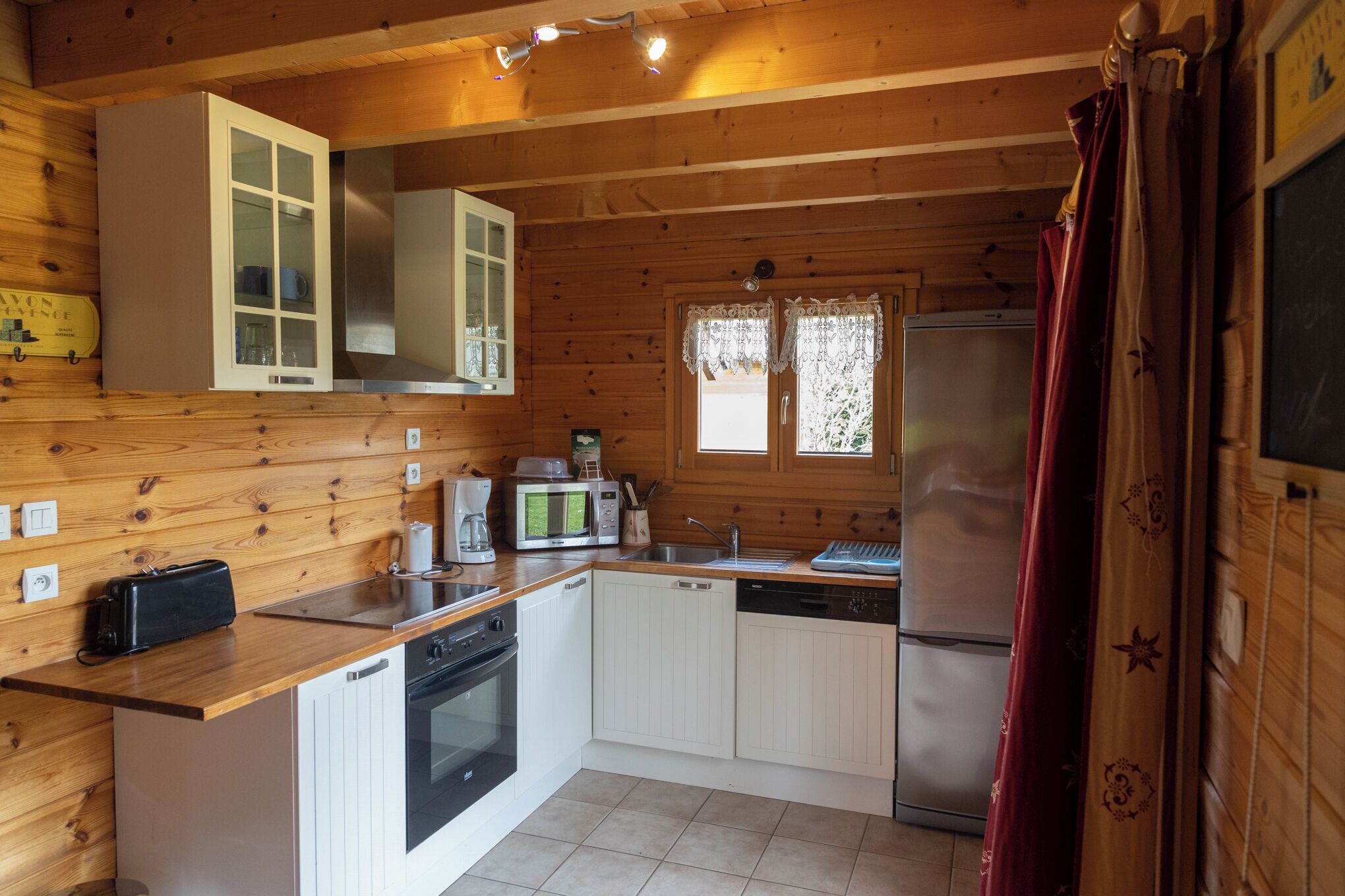Cocina compacta con paredes de madera, microondas, refrigerador, lavamanos y lavavajillas.