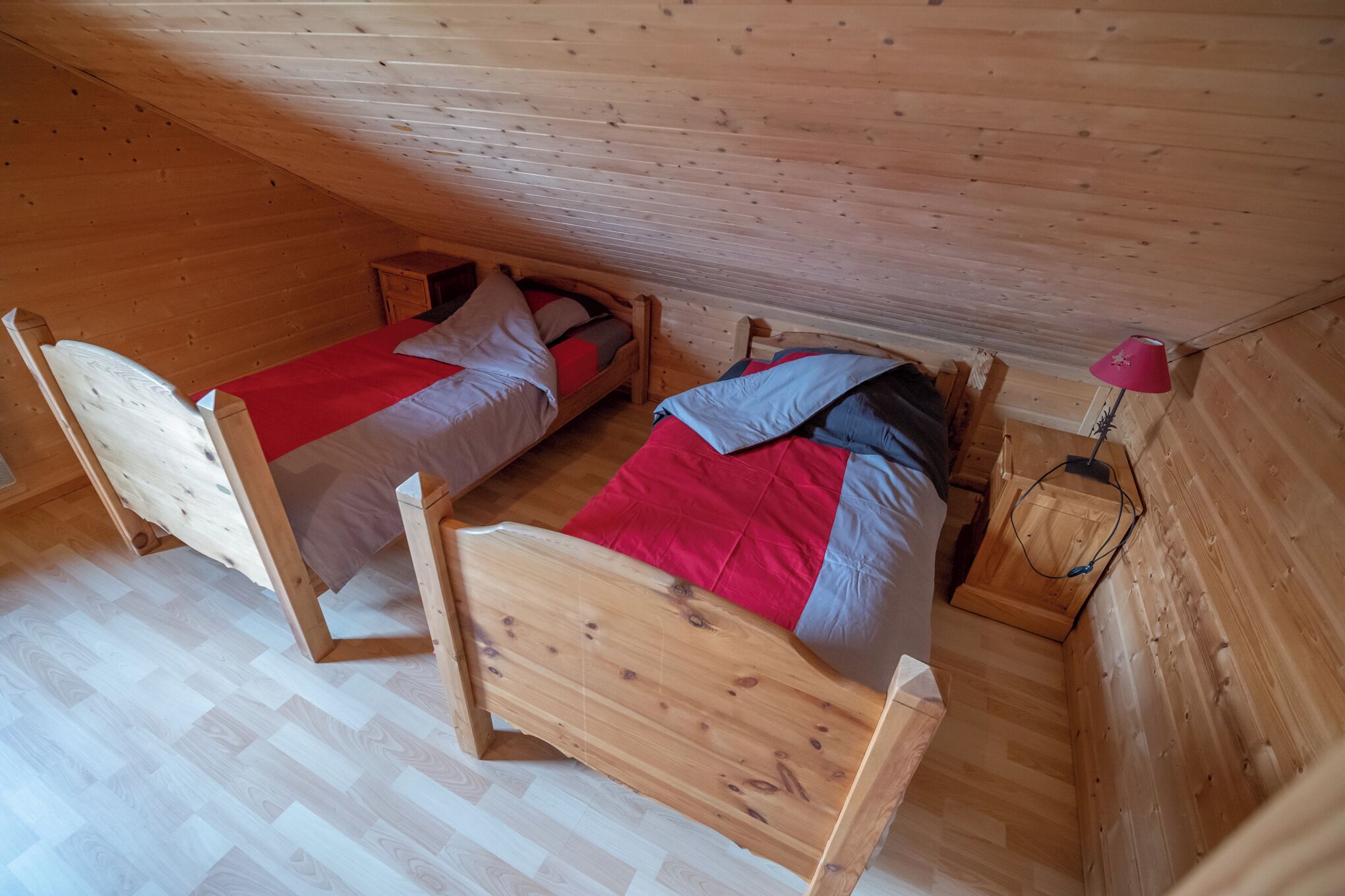 Ein kleiner, holzgetäfelter Raum mit zwei Betten, einem Nachttisch und einer roten Lampe.