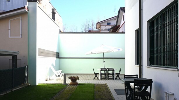 A patio with a table and chairs, a white umbrella, and a small garden area.
