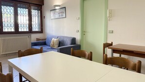 A room with a dining table, chairs, a sofa, a green door, and a window with a view.