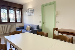 A room with a dining table, chairs, a sofa, a green door, and a window with a view.