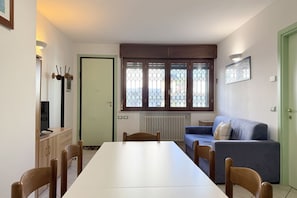 A dining area with a table, chairs, a sofa, a radiator, and a window with a view.