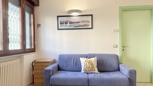 A room with a blue sofa, a wooden cabinet, a radiator, a framed painting, and a green door.