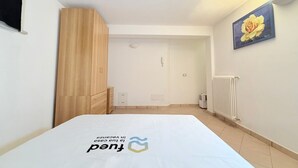 A bedroom with a bed, a wooden wardrobe, a radiator, and a painting on the wall.