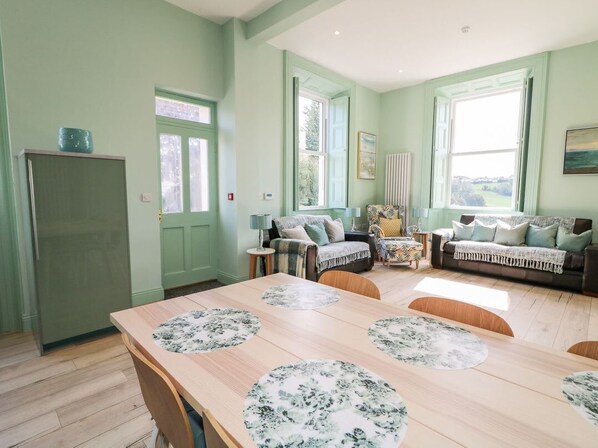 A dining area with a wooden table and chairs, a green door, and a window with a view.