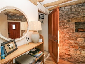 A wooden console table with a mirror, lamp, framed picture, and books. A stone wall and wooden door are visible in the background. - Holme Fell View is in Sedbergh (Sedbergh)