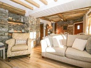 A cozy living room with a stone fireplace, wooden beams, a sofa, and a chair. - Holme Fell View is in Sedbergh (Sedbergh)