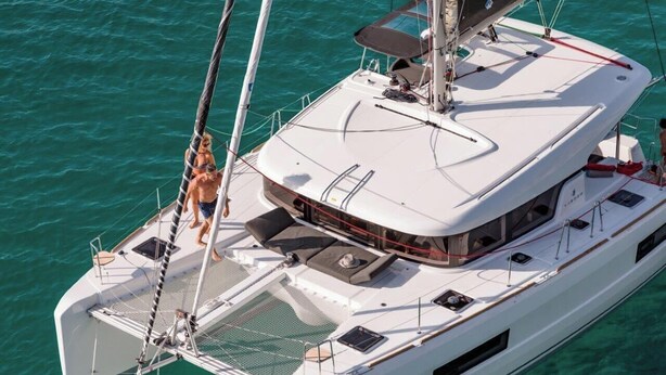 En vit yacht med ett täckt däck, en mast och en person som står på fördäcket.