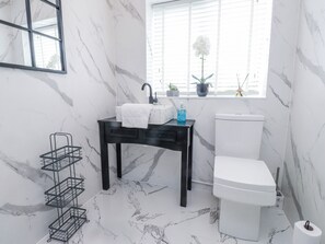 Ein Badezimmer mit Marmorboden, einem schwarzen Waschtisch mit Spüle, einer Toilette und einem Fenster mit Jalousien.