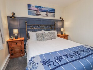 Ein ordentlich bezogenes Bett mit einem gemusterten Überwurf, zwei Nachttische mit Lampen, ein an der Wand hängendes Bild von Segelbooten und ein dunkelblaues Kopfteil.