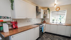 Een keuken met witte kastjes, een houten aanrechtblad, een gasfornuis en een raam met jaloezieën.
