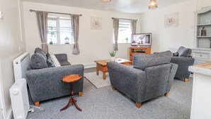 Een moderne woonkamer met grijze banken, een houten salontafel, een tv op een houten meubel en een radiator.