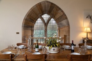 A dining table set with plates, glasses, and a bottle of wine, with a window and a lamp in the background. - Greystead Old Church, Bellingham (Hexham)