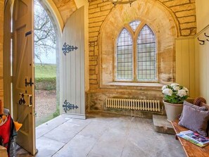A stone-walled room with a large arched window, a radiator, and a bench with a cushion. - Greystead Old Church, Bellingham (Hexham)