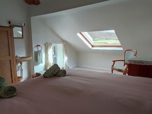 A bedroom with a skylight, a bed, a chair, a dresser, and a window with curtains.