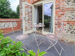 A patio with a table and chairs, a glass door leading to a room, and a brick wall with a stone pattern.