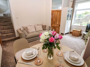 Un coin repas avec une table dressée pour deux personnes, un vase de fleurs et un escalier en arrière-plan.