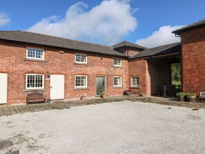 A brick building with multiple windows, a gravel courtyard, and a covered area.