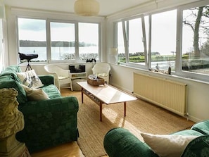 A living room with a green sofa, a white armchair, a small table, and large windows overlooking a body of water.
