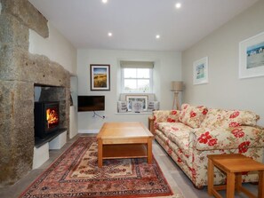 Una sala de estar con chimenea de piedra, un sofá, una mesa de centro, un tapete y un televisor.