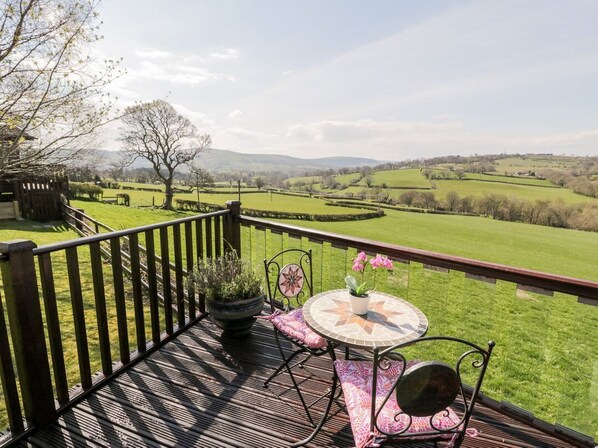 A deck with a table and chairs, overlooking a green landscape with fields and trees.