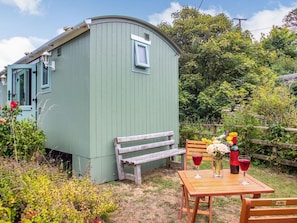Ein grüner Holler Schuppen mit einer Bank und einem Tisch, dekoriert mit Blumen und Weingläsern.