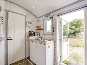 A compact kitchen with white cabinets, a stove, and a window overlooking a garden. - The Shepherd's Hut, Aberdovey (Aberdovey)