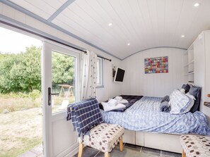 A bedroom with a bed, a chair, a TV, and a window. - The Shepherd's Hut, Aberdovey (Aberdovey)