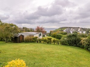 Une propriété rurale dotée d’une pelouse verdoyante, d’un petit abri de jardin et d’une maison avec un toit en pente.