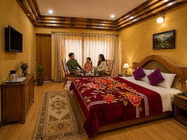 Habitación de hotel con cabecera de madera, colcha de cama estampada con motivos florales, televisor en la pared y un cuadro sobre la cama.