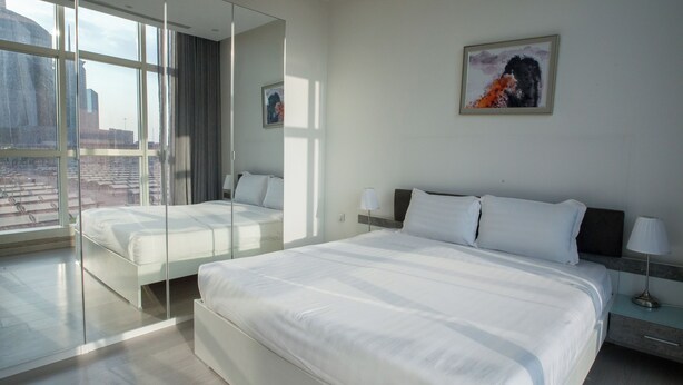 A modern hotel room with a large bed, a bedside table, a mirror, and a city view. - Darent Royal Two Bedroom Kafd View Al Ghadir (Riyadh)