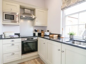 Una cocina con armarios blancos, un microondas de acero inoxidable, un horno empotrado, una encimera negra y una ventana con vistas al exterior.