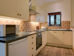 Una cocina compacta con armarios blancos, microondas, hervidor y ventana.