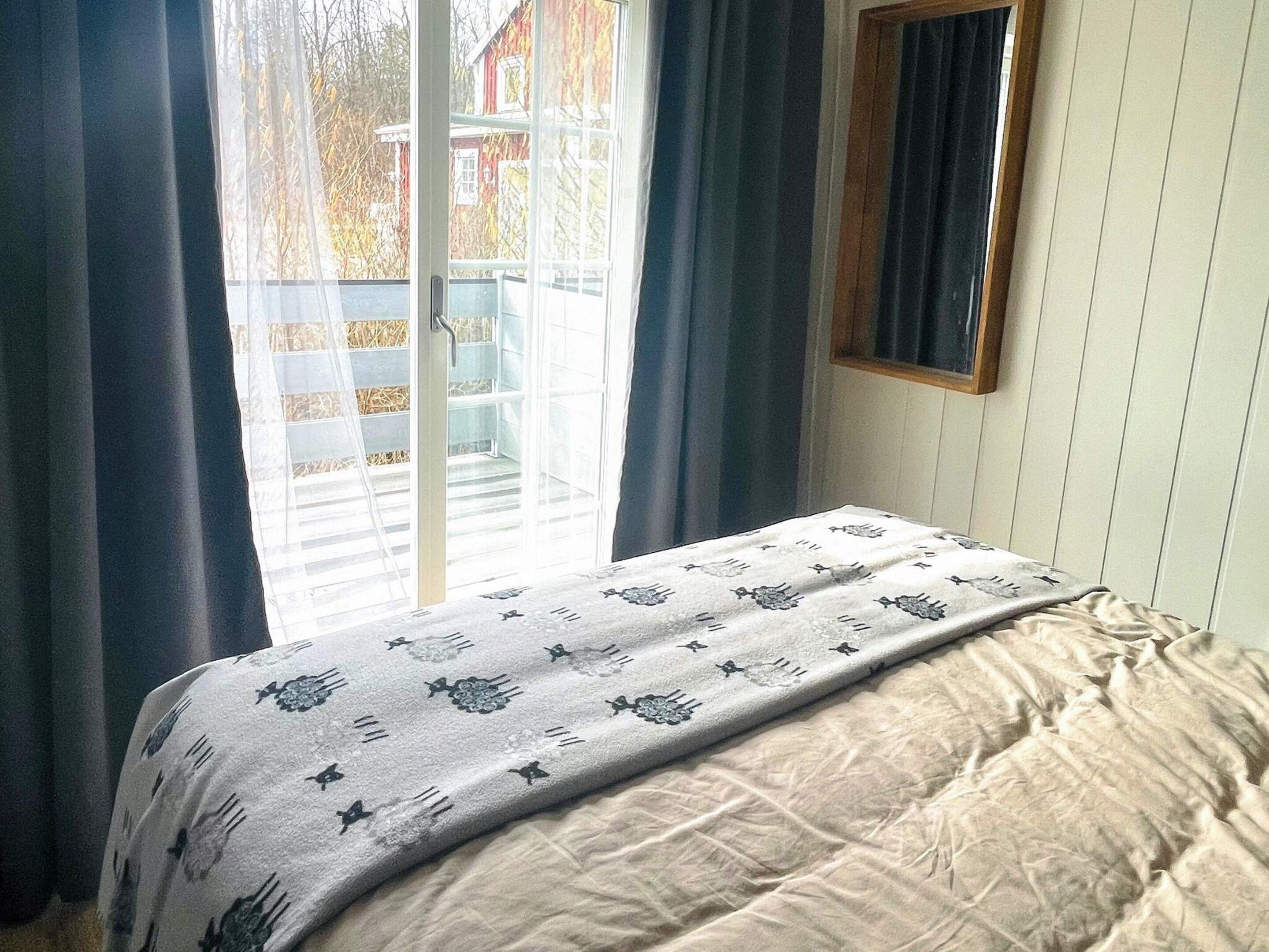 A bedroom with a bed, a window with curtains, and a view of a building outside.