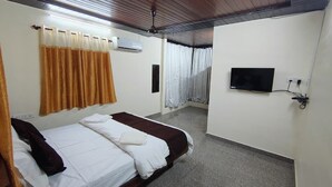 A hotel room with a bed, curtains, an air conditioning unit, a television, and a ceiling fan. - Shelar Agro Tourism and Holiday Homes (Mahabaleshwar)