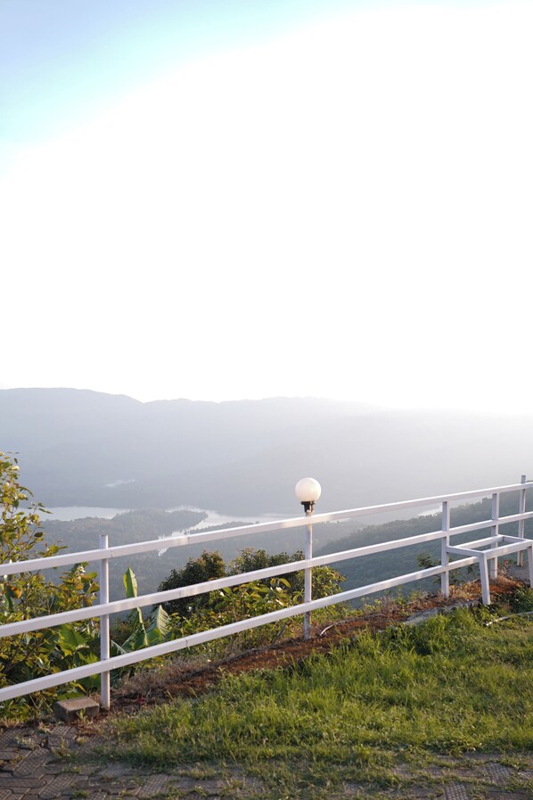 A white metal railing with a spherical light fixture, overlooking a body of water and distant mountains. - Shelar Agro Tourism and Holiday Homes (Mahabaleshwar)