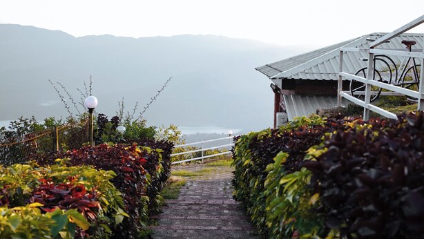 A pathway leading to a building with a bicycle rack, surrounded by lush greenery and a view of distant mountains. - Shelar Agro Tourism and Holiday Homes (Mahabaleshwar)