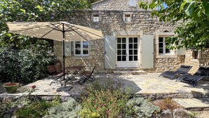 Ein Steinhaus mit Terrasse, Sitzgelegenheiten im Freien und einem großen Sonnenschirm.