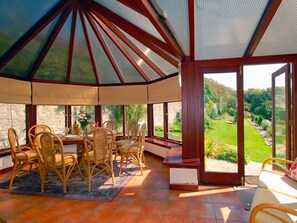 A covered patio with a dining table and chairs, large windows, and a view of a garden.